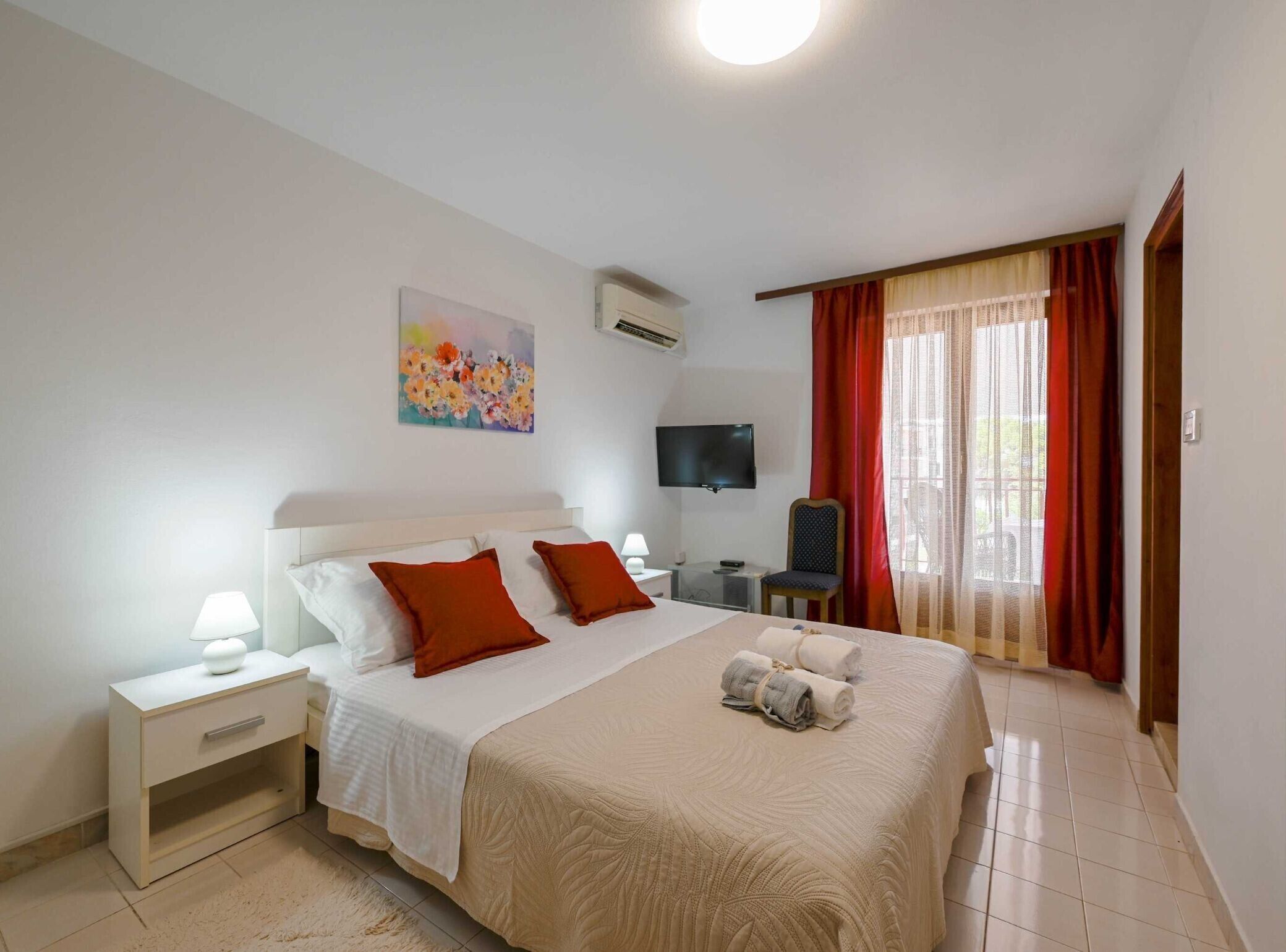 A hotel room with a large bed, a bedside table, a TV, and a window with curtains.