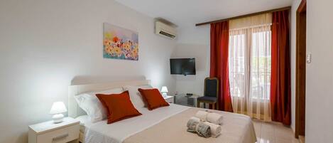 A hotel room with a large bed, a bedside table, a TV, and a window with curtains.