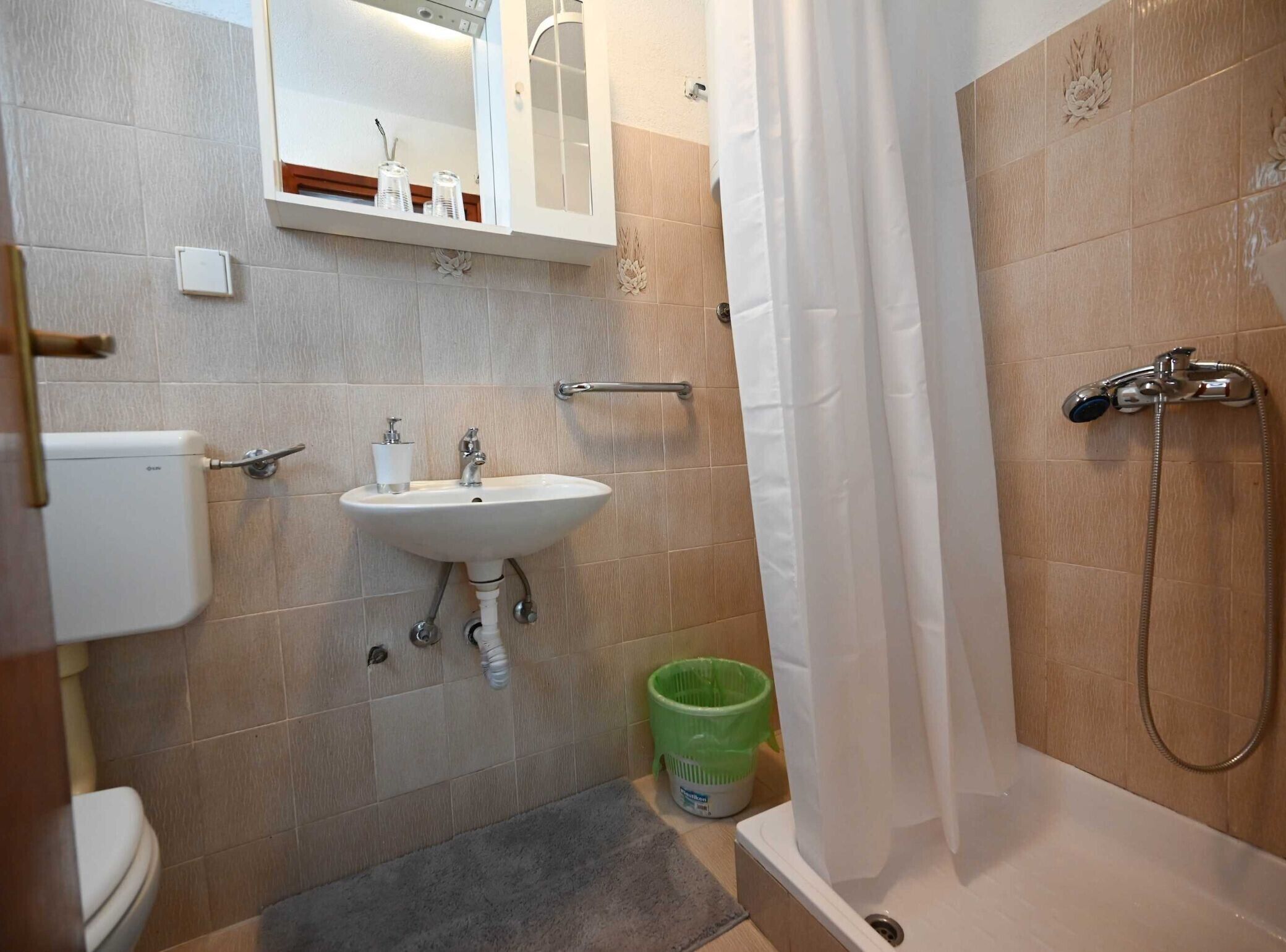 Un baño con lavabo, inodoro, ducha y un cubo de basura verde.