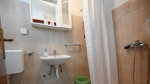 A bathroom with a sink, toilet, shower, and a green trash bin.