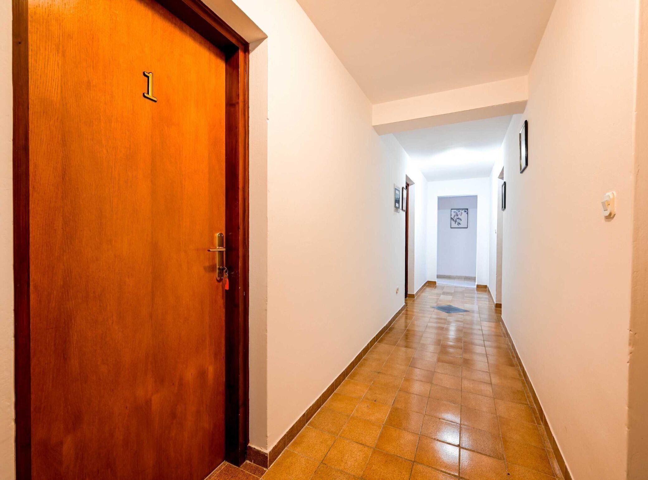 A hallway with a wooden door marked '1', white walls, and a tiled floor.
