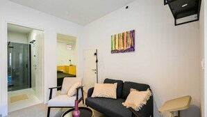 Un salon moderne avec un canapé, un fauteuil et une petite table sur laquelle est posé un vase. Un tableau orne le mur et un luminaire est fixé au plafond.