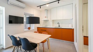 Une cuisine moderne avec des meubles blancs, un luminaire suspendu noir et un four encastré.