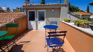 Une terrasse sur le toit avec une petite table et des chaises, une porte et des plantes en pot.