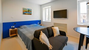 Une chambre avec un lit, un canapé, une télévision et un tableau au mur.