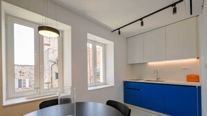 Une cuisine moderne avec des meubles blancs et bleus, une table à manger noire et des luminaires suspendus.