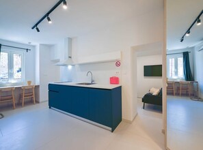Kitchen area with central island, sink, and range hood, adjacent to a living space with sofa and TV.