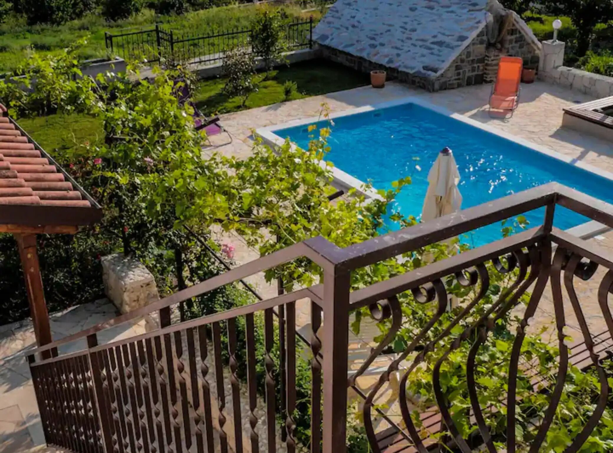 A pool area with a stone house, a pergola, and a fenced deck.