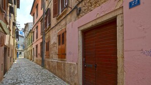 Une ruelle étroite pavée, bordée de bâtiments aux volets en bois et d’un mur rose orné d’un numéro.