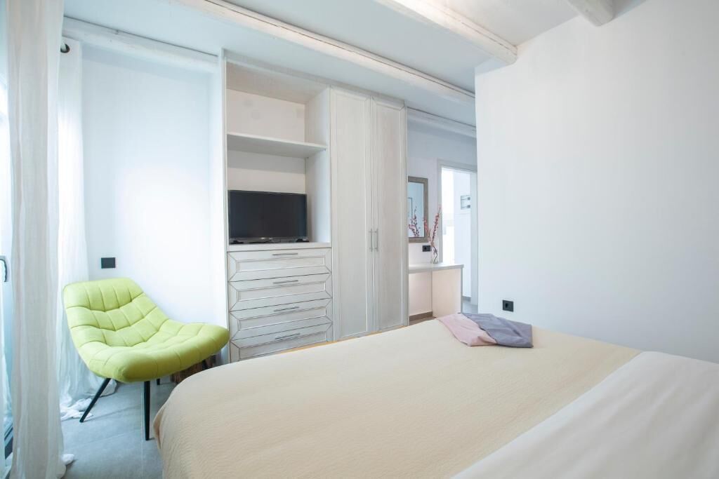 Moderni hotellihuone, jossa on sänky, vihreä tuoli, televisio ja vaatekaappi.