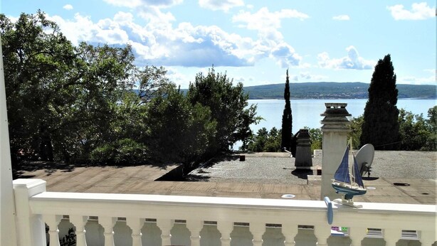 Un balcon avec une table et des chaises, donnant sur une étendue d’eau et des arbres.