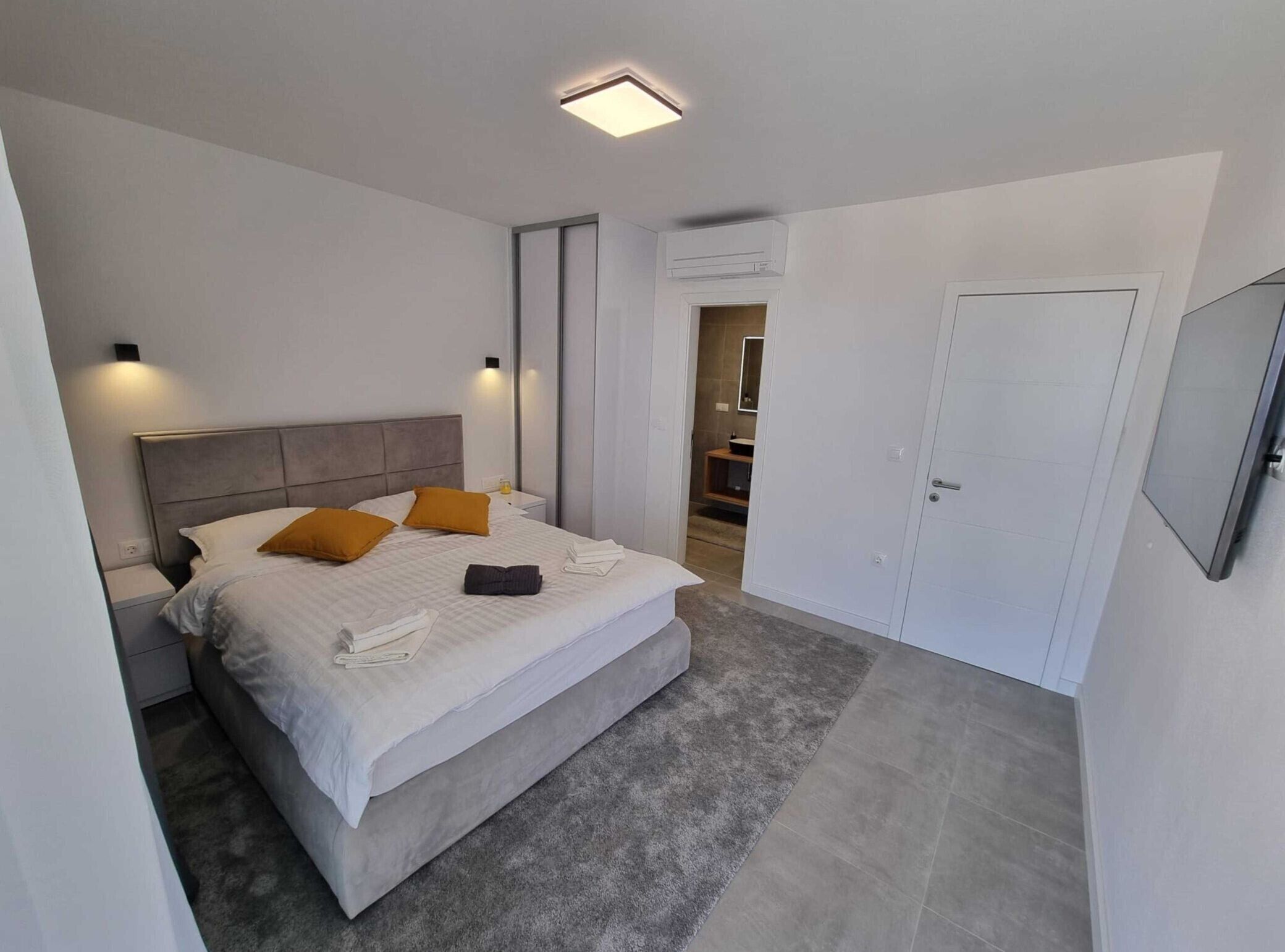 A modern bedroom with a large bed, bedside tables, a wardrobe, and a bathroom visible through an open door.