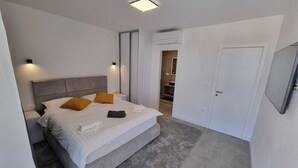Ein modernes Schlafzimmer mit einem großen Bett, Nachttischen, einem Kleiderschrank und einem durchgehenden Türbogen sichtbarem Badezimmer.