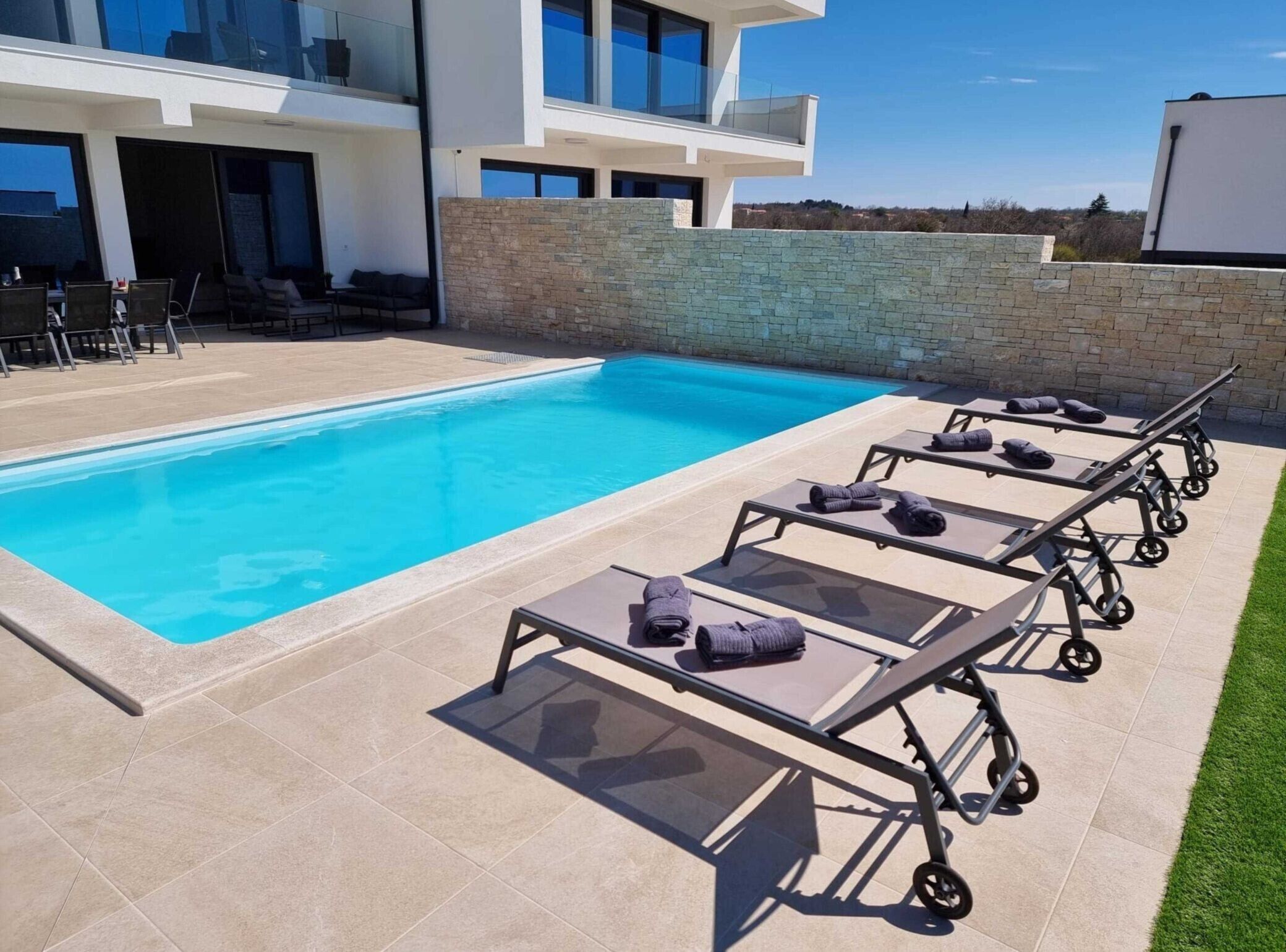 Ein moderner Poolbereich mit klarem, blauem Pool, Liegestühlen und einer Steinwand.