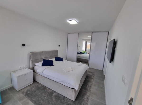 A modern bedroom with a large bed, a nightstand, a TV, and a mirror.