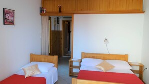A room with two wooden beds, each with a red bedspread and white linens. There is a wooden cabinet above the beds, a small bedside table with a lamp, and a framed picture on the wall. - Sweet and Simple Sea view Crikvenica Apartments - One Bedroom Apartment withe Sea view and Balcony (Crikvenica)