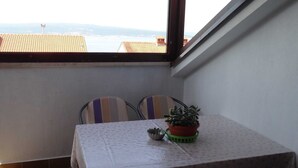 En balkon med et bord og stole, en potteplante og udsigt til bygninger og vand.