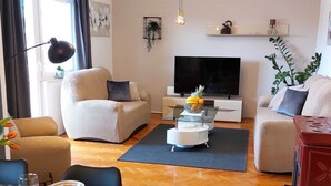 Ein modernes Wohnzimmer mit einer Couch, einem Esstisch für zwei Personen, einem Flachbildfernseher und einem Couchtisch mit Obst.