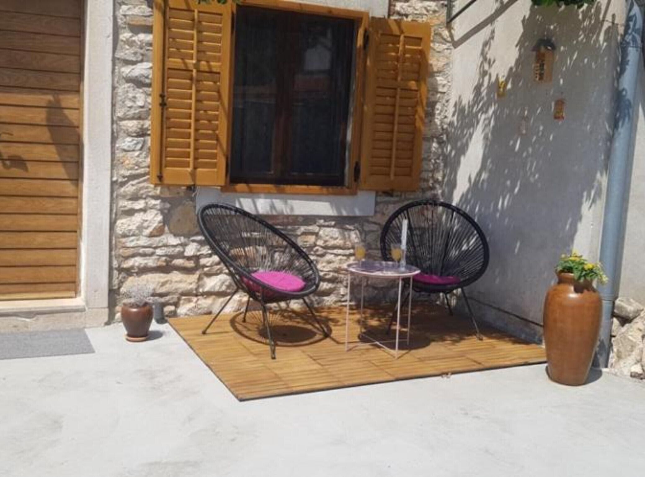 Een terras met twee zwarte rieten stoelen, een kleine ronde tafel, een plant in pot en een stenen muur.