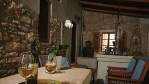 Une pièce aux murs de pierre, avec une table en bois, deux verres de vin et une orchidée en pot.