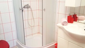 A bathroom with a glass-enclosed shower, a white sink with red towels, and a red toilet. - One Bedroom Apartment with Terrace (Crikvenica)