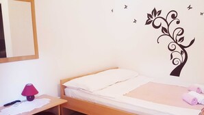 A small, neatly made bed with white linens and a pink blanket, a wooden nightstand with a red lamp, and a wall decal of a tree with birds. - One Bedroom Apartment with Terrace (Crikvenica)