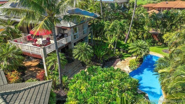 A tropical resort with a pool, palm trees, and a deck with outdoor furniture.