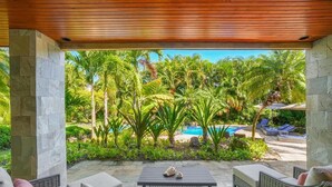 A covered outdoor area with a pool, lounge chairs, and tropical plants.