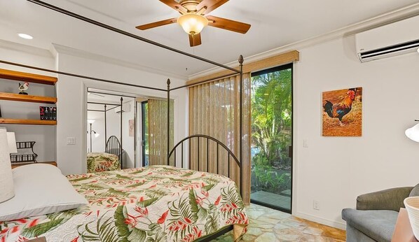 A bedroom with a bed, a ceiling fan, a window with curtains, a door leading to a balcony, and a wall-mounted air conditioner.