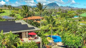 A house with a solar panel roof, a pool, and a lush garden.