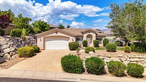 A single-story house with a garage, surrounded by well-maintained landscaping and a clear blue sky. - Home w/ Game Room: Near Zion National Park! (Hurricane)