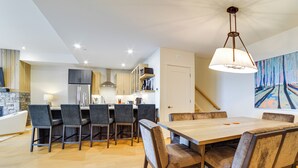 Une cuisine moderne avec un îlot central, des chaises foncées et une table à manger en bois.
