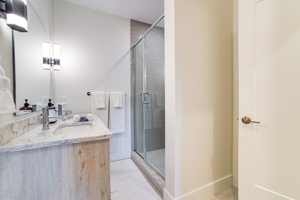 A modern bathroom with a marble sink, a glass shower enclosure, and a large mirror.