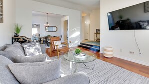 A modern living room with a grey sofa, a glass coffee table, and a TV mounted on the wall. - Outdoor Oasis & Game Room: Henderson Retreat (Henderson)
