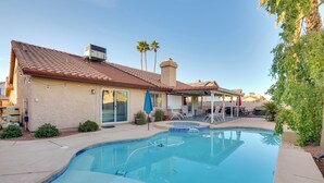 A swimming pool with a tiled deck, a covered patio area, and a building with a tiled roof and a chimney. - Outdoor Oasis & Game Room: Henderson Retreat (Henderson)