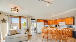 A spacious living area with a sofa and chairs, a kitchen with wooden cabinets and a refrigerator, and a large window with curtains. - 1 Mi to Story Land: Spacious Home w/ Mtn Views! (Bartlett)