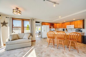Ein geräumiger Wohnbereich mit einer Couch und Sesseln, eine Küche mit Holzschränken und einem Kühlschrank, sowie ein großes Fenster mit Vorhängen.