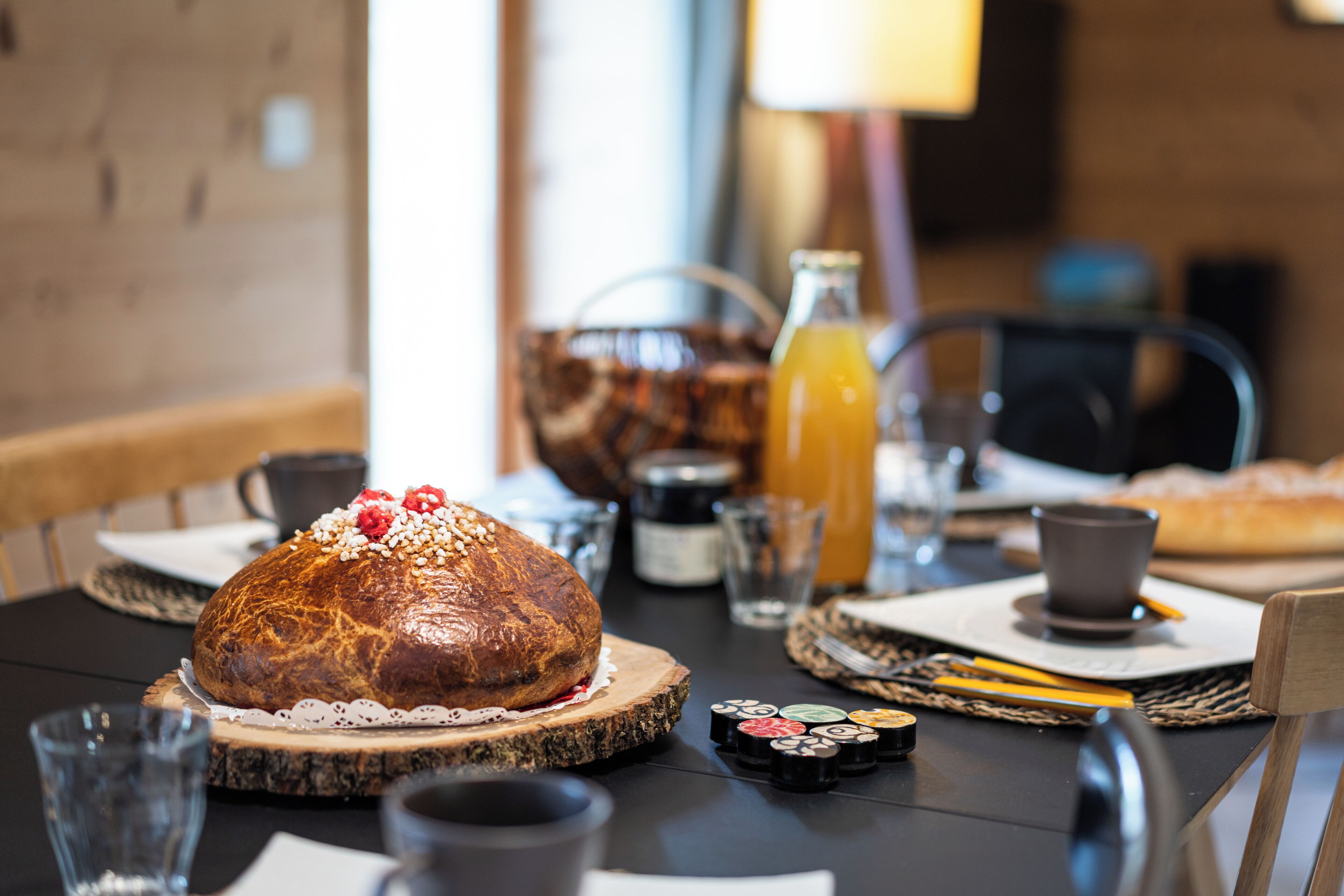Una mesa de comedor con un pan grande, una botella de jugo de naranja y diferentes condimentos.