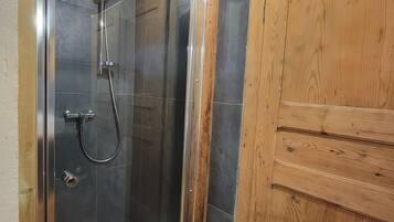 A shower area with a glass door, wooden ceiling beams, and a wooden door.