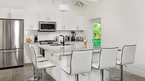 Een moderne keuken met witte kastjes, roestvrijstalen apparatuur, een granieten aanrecht en barstoelen.