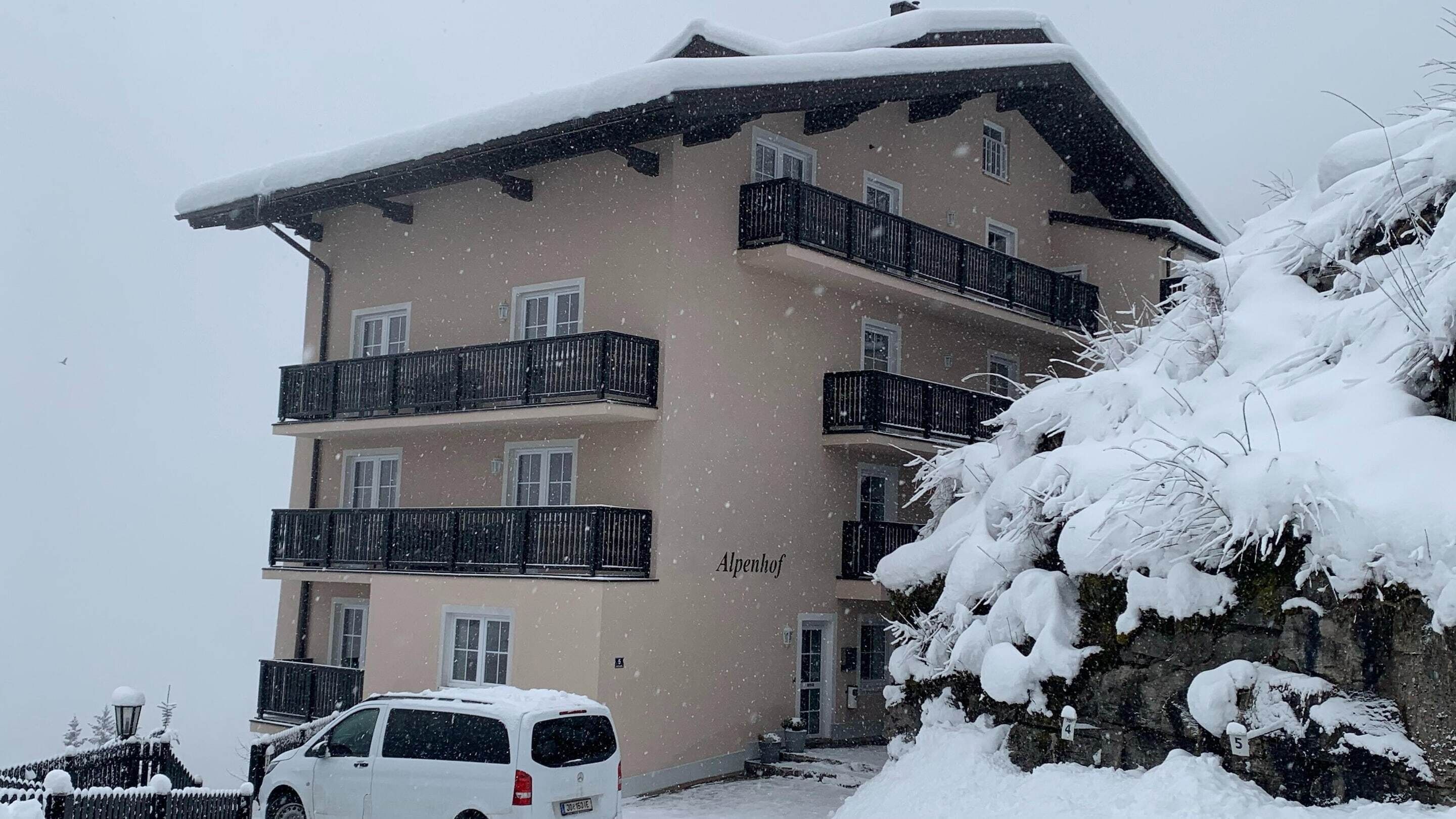 A multi-story building with balconies, snow-covered surroundings, and a car parked in front.