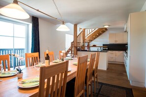 A dining area with wooden chairs and a table set for a meal, a kitchen with white cabinets, and a staircase leading to an upper level. - Picturesque Apartment in Salzburg (Bad Gastein)