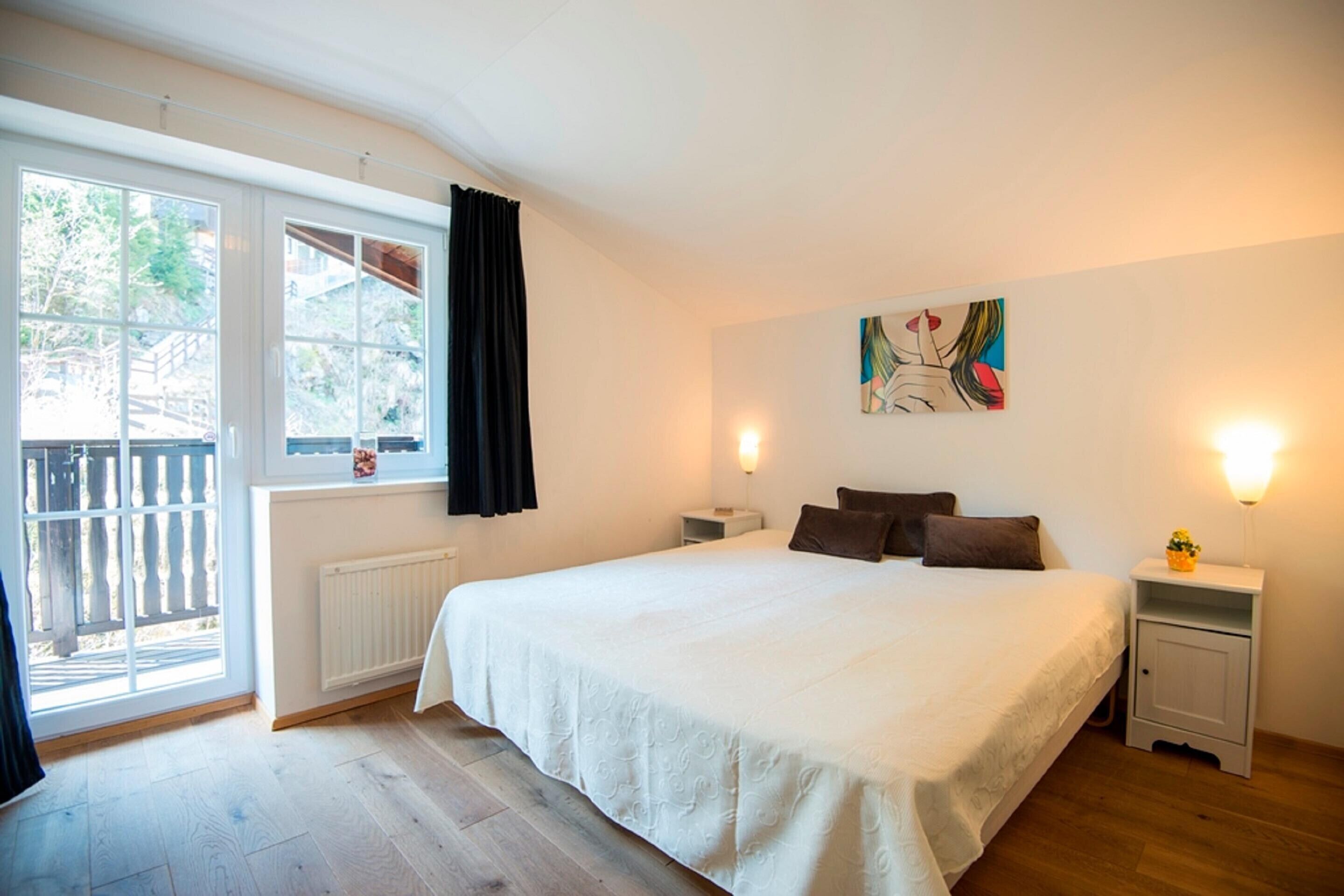 A bedroom with a large bed, a window with curtains, a radiator, and a painting on the wall.