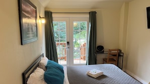 A bedroom with a bed, a desk, and a view of the outdoors through a door.