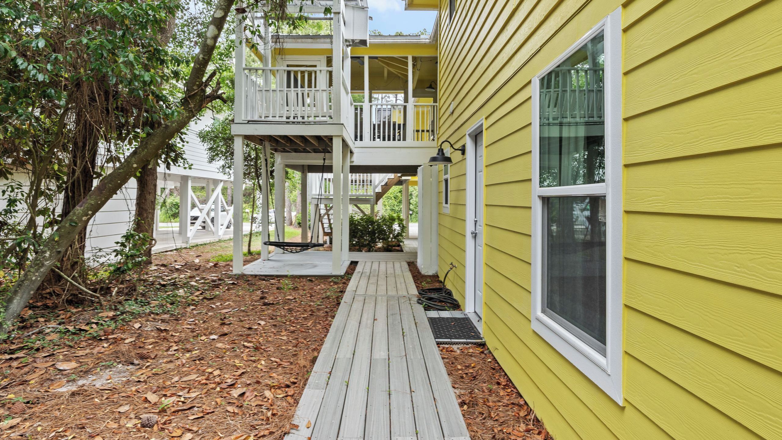 A yellow building with a wooden deck, a covered porch, and a staircase leading to a second floor.