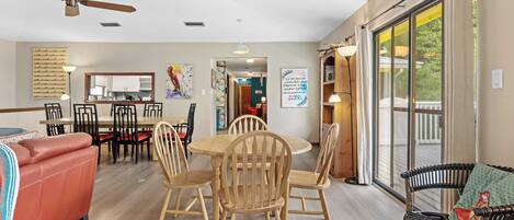 A spacious living area with a dining table surrounded by chairs, a sofa, and a large window with a view.