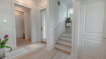 Un pasillo con paredes blancas y pisos de madera, que conduce a una escalera con una planta en el rellano.