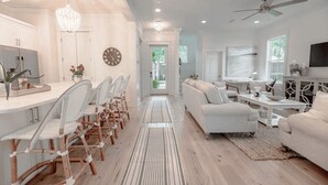 A modern living room with a sofa, a dining area with chairs, a TV, and a ceiling fan.