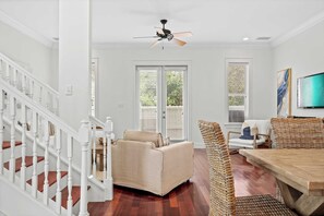 A spacious living room with a sofa, wicker chairs, a wooden dining table, and a ceiling fan. - Dragonfly Dreams 30A by Avantstay Walk to Beach (Panama City Beach)
