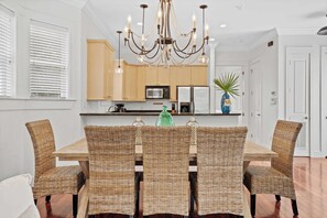 A dining area with a wooden table and wicker chairs, a chandelier, and wooden cabinets. - Dragonfly Dreams 30A by Avantstay Walk to Beach (Panama City Beach)